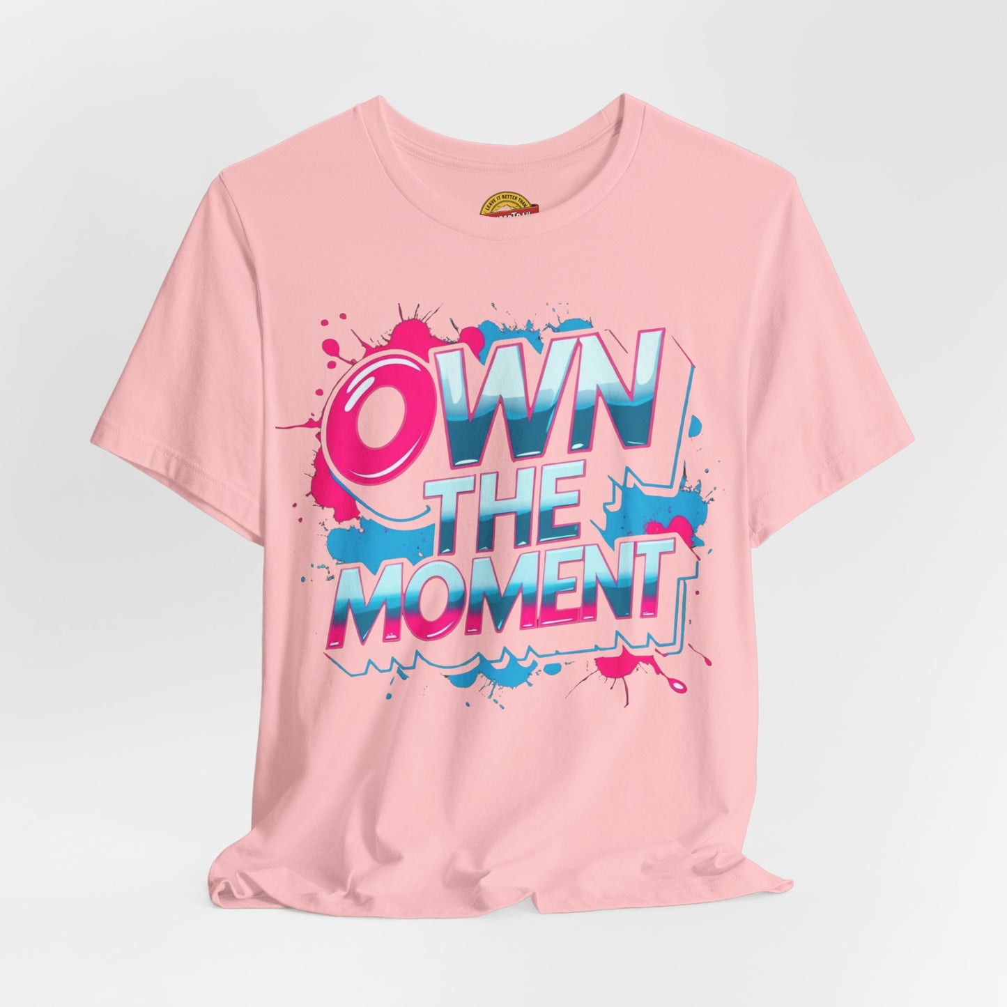 Pink t-shirt with 'OWN THE MOMENT' text on a light gray background