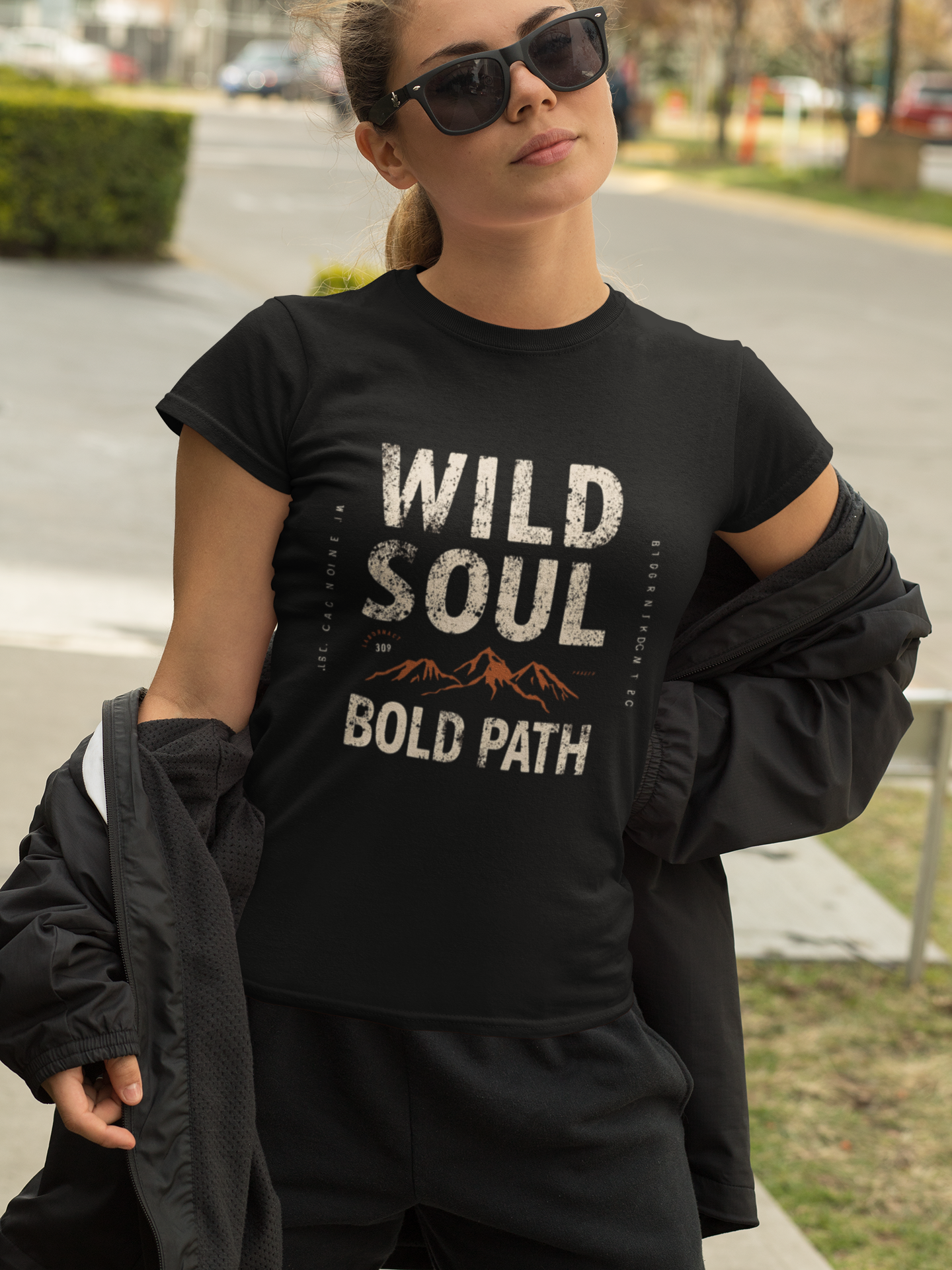 Woman wearing a black t-shirt with 'Wild Soul Bold Path' text outdoors.