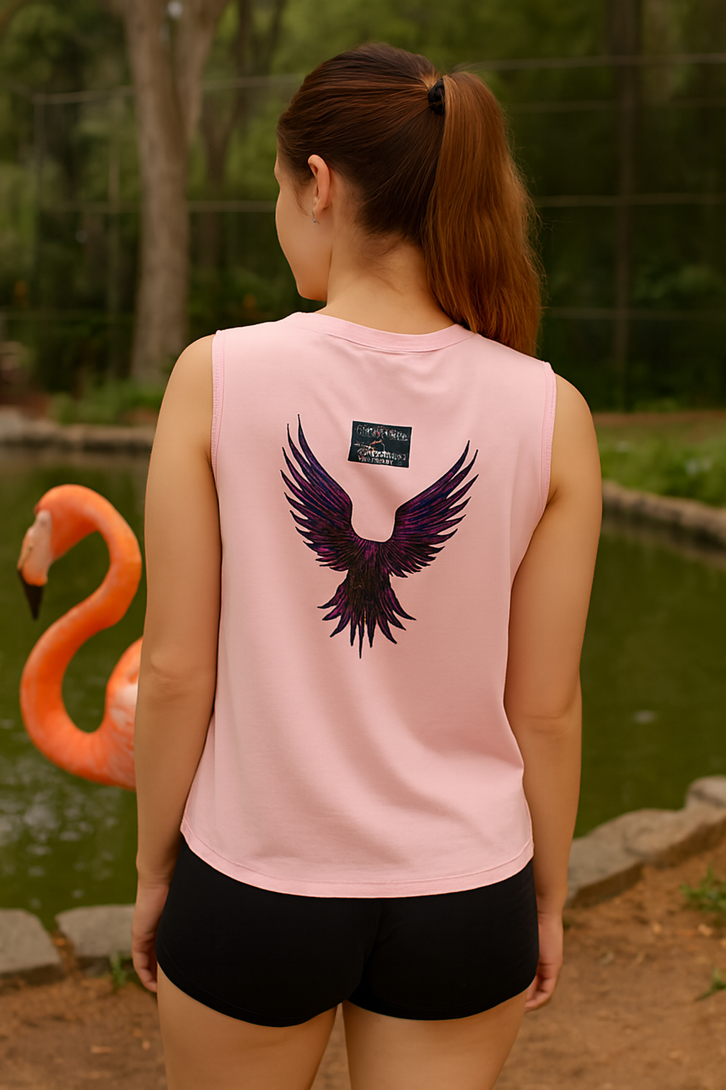 Person wearing a pink sleeveless shirt with an eagle design outdoors near a flamingo.