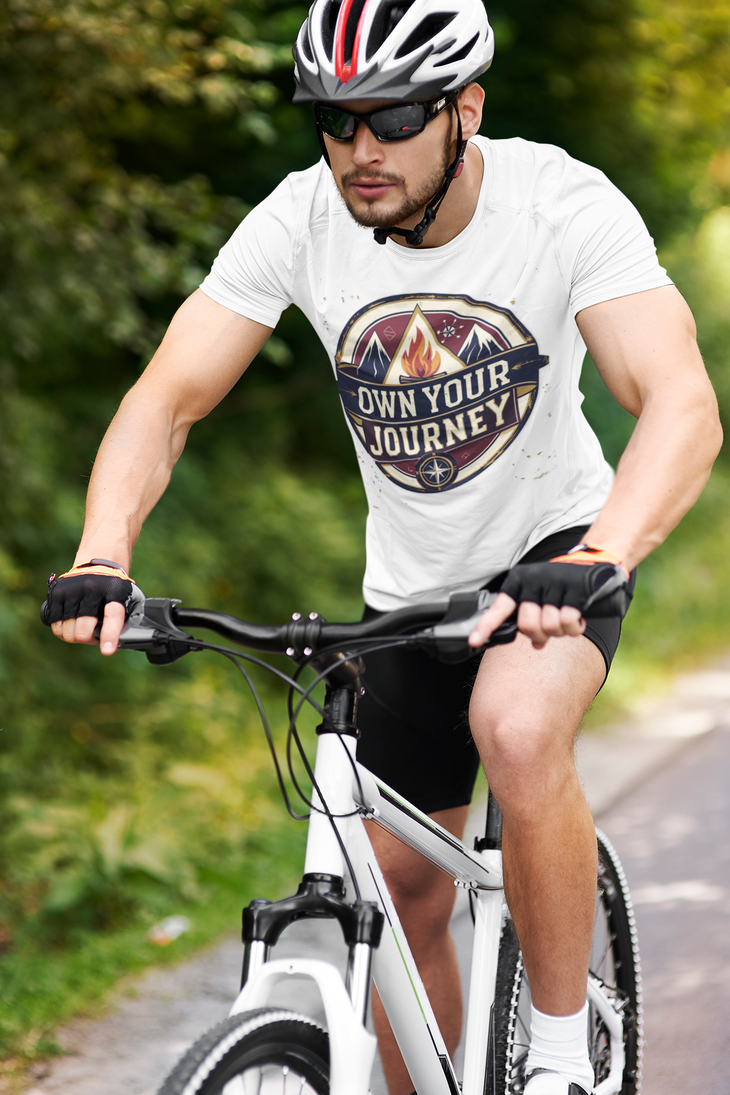Man riding a bicycle on a path with a 'Own Your Journey' t-shirt.