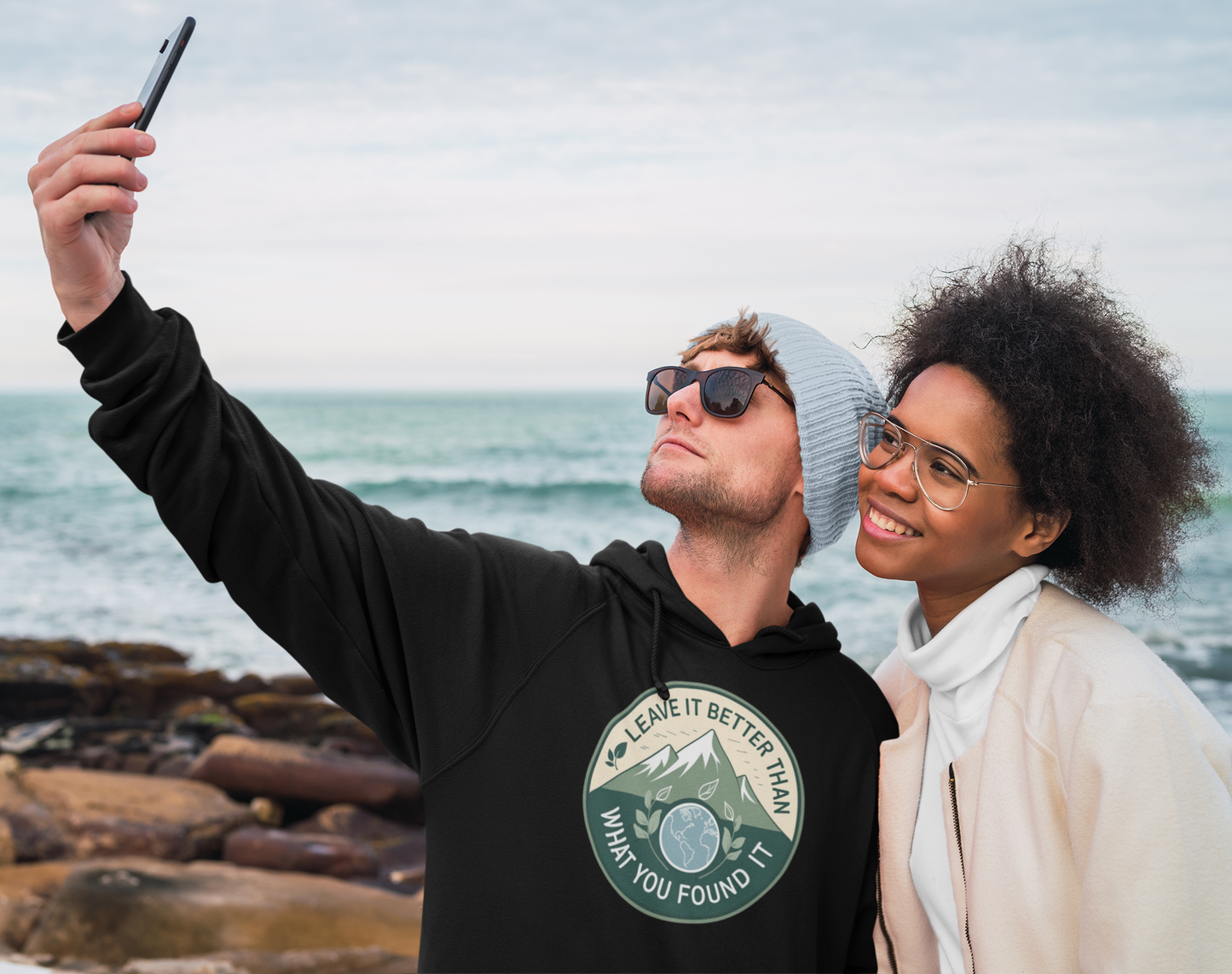 Two people taking a selfie on a rocky shoreline with ocean in the background.