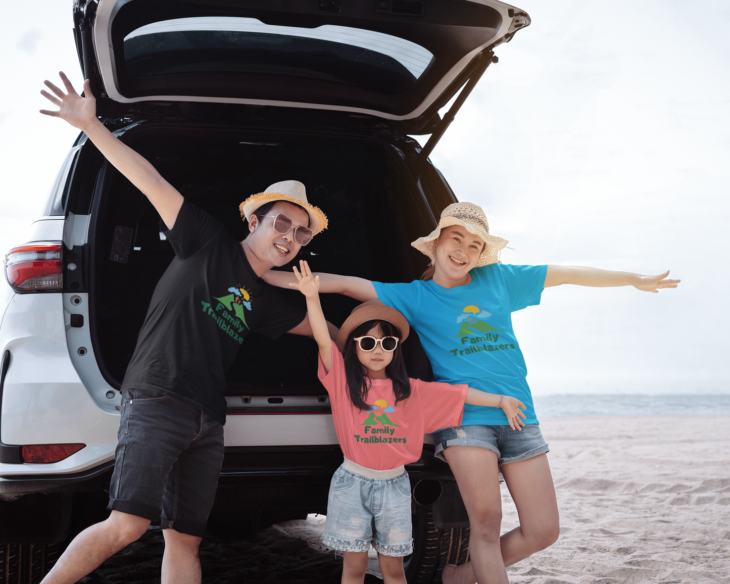 Three people posing in front of an open car trunk on a beach.