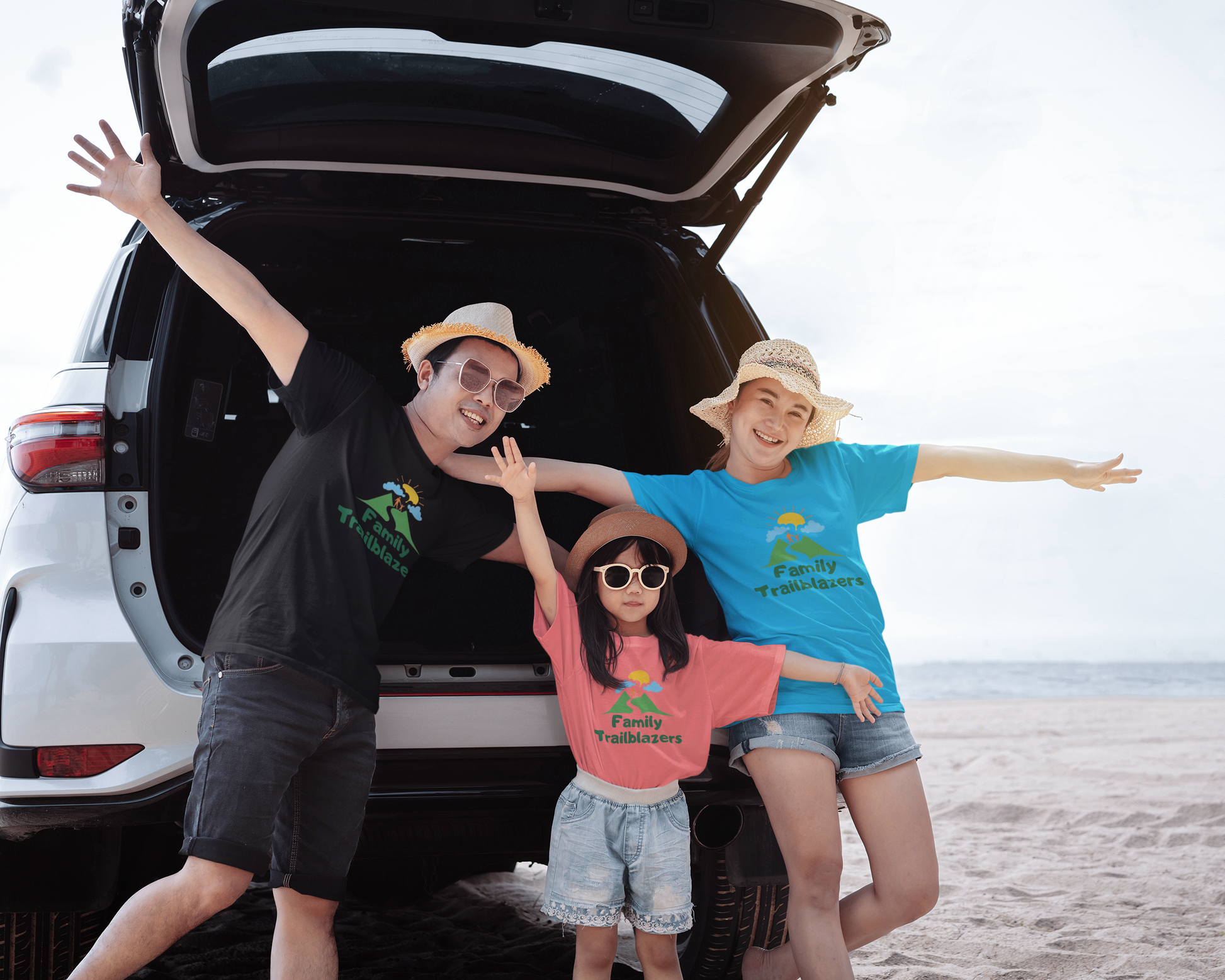 Three people posing in front of an open car trunk on a beach.