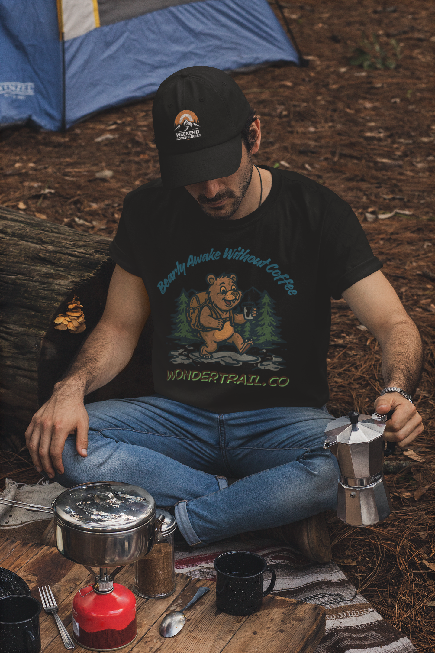Man sitting outdoors by a camping setup with a coffee percolator and snacks.