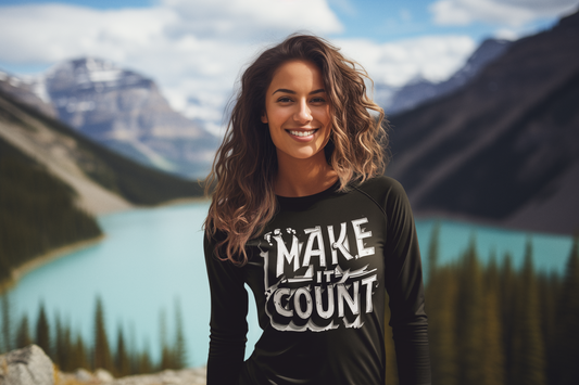 Woman wearing a black t-shirt with 'MAKE IT COUNT' text in front of a mountain lake landscape