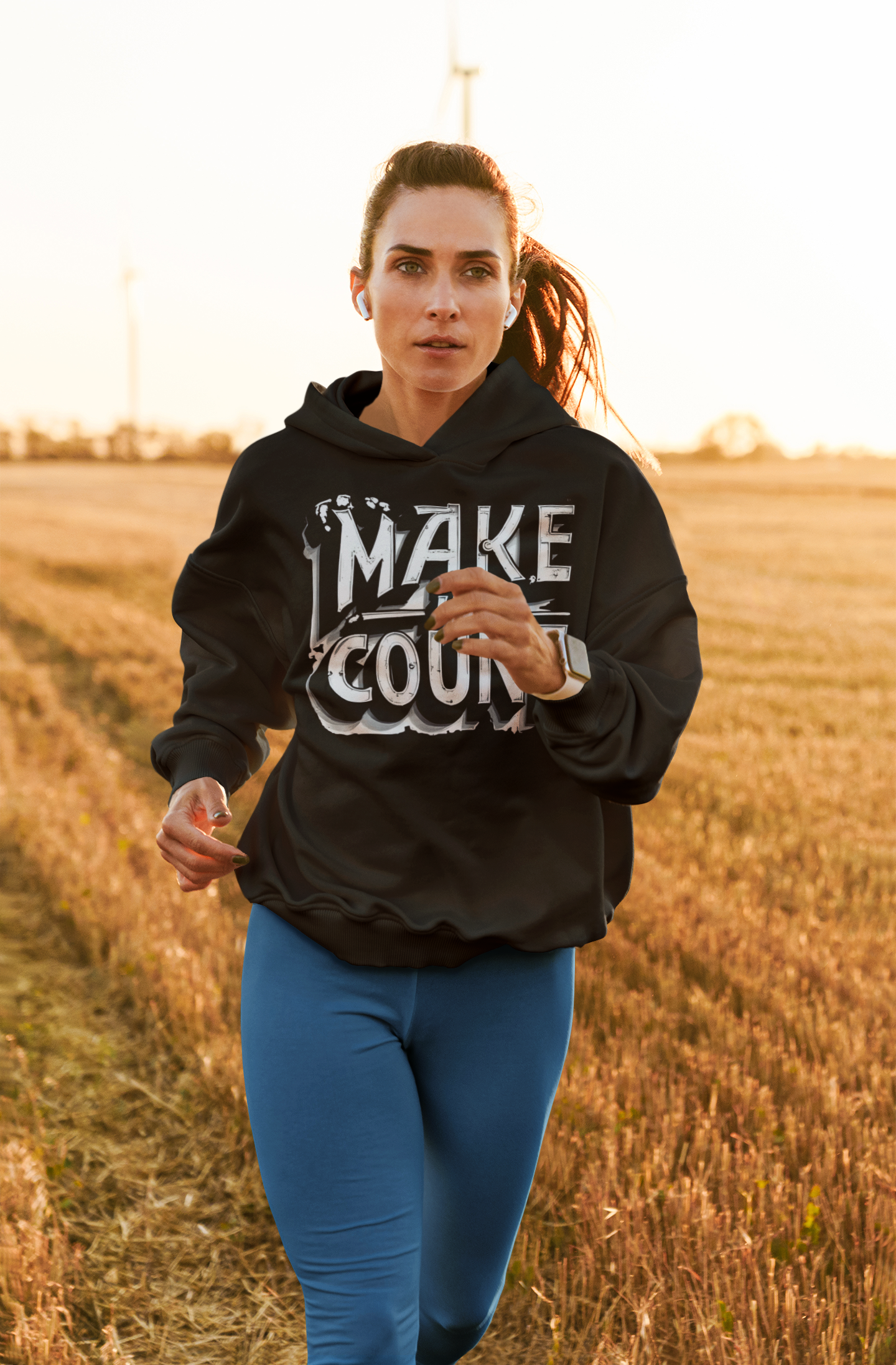 Woman running in a field wearing a black hoodie with text and blue leggings.