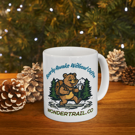 White mug with bear graphic and text on a wooden surface with pinecones and a Christmas tree in the background