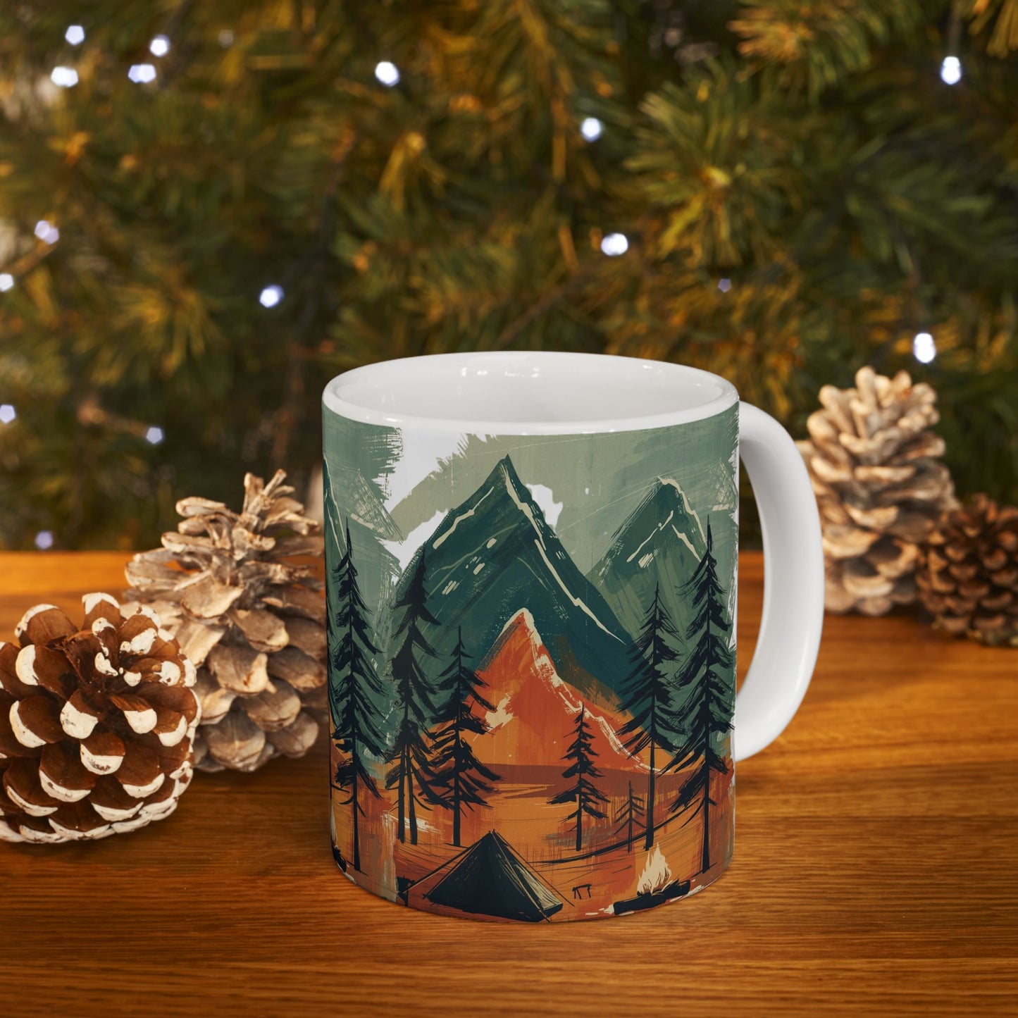 Ceramic outdoor mug with mountain and forest design, tent and campfire artwork, styled in winter holiday scene — eco-friendly rustic gift for campers and nature lovers
