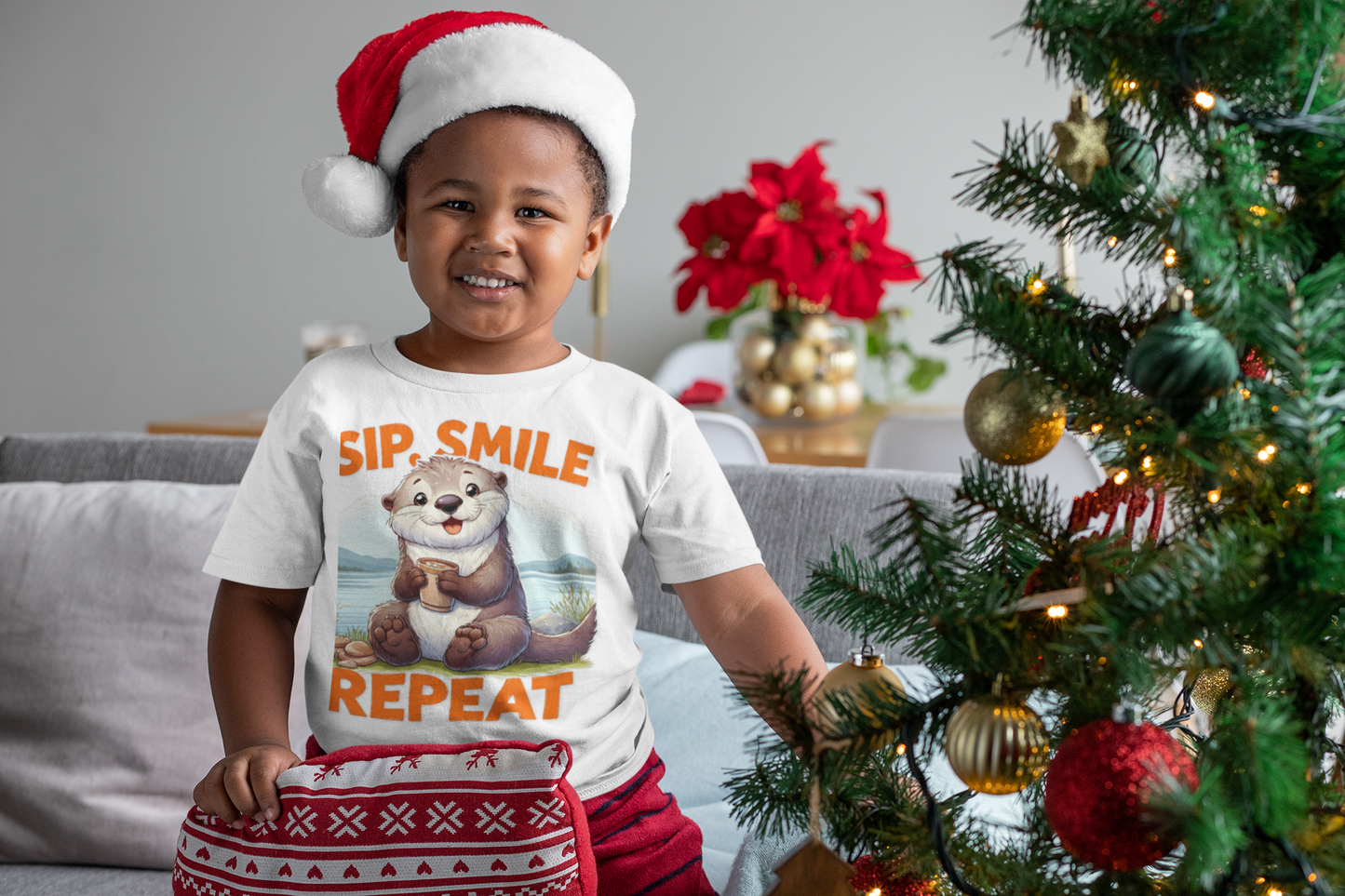 Festive kids’ Christmas T-shirt with cheerful otter illustration and Sip Smile Repeat slogan, WonderTrail.Co holiday apparel for family celebrations, gifting, and nature lovers.