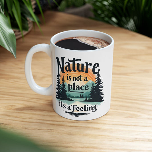 White ceramic mug with colorful mountain, trees, and sunset design plus inspirational Nature Is Not a Place It’s a Feeling slogan — WonderTrail.Co outdoor lifestyle drinkware for hikers, campers, nature lovers, and gifting.