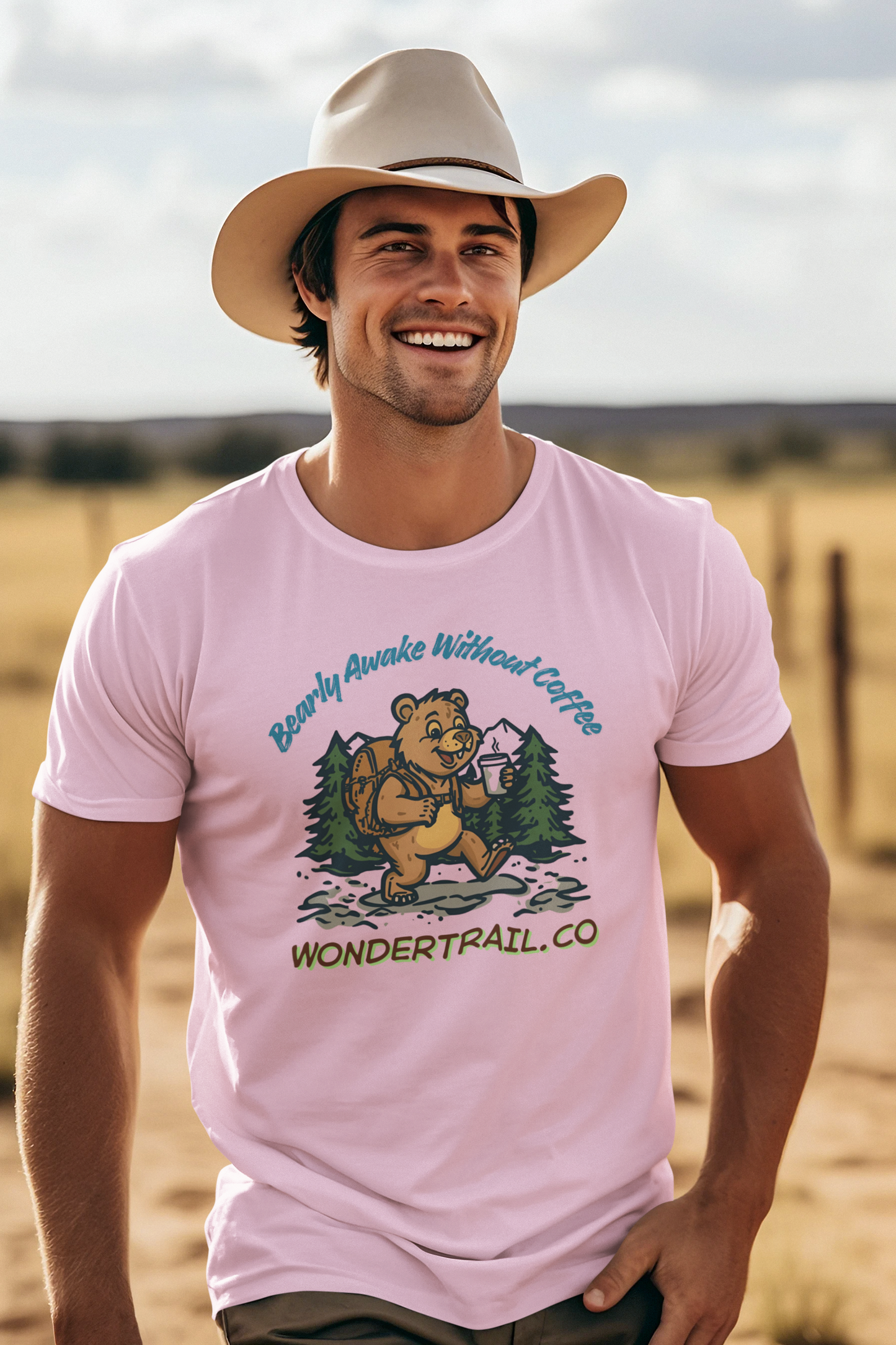 Man wearing a pink t-shirt with a bear graphic and text, standing in a desert landscape.